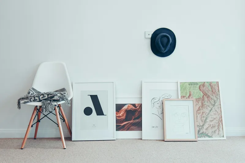 A minimalist interior with a white wall and floor, featuring art and furniture